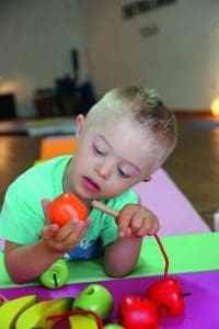 enfant avec une trisomie joue avec des grosses perles